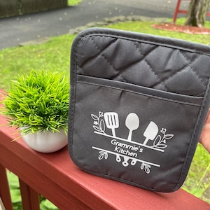 May include: Gray quilted oven mitt with a white design of kitchen utensils and the text "Grammy's Kitchen".