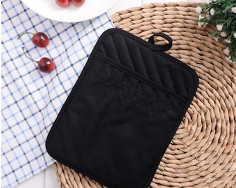 May include: A black quilted oven mitt with a pocket, featuring a loop for hanging. The mitt is on a woven placemat, with a checkered cloth and a plate of cherries in the background. The mitt is designed for kitchen use.