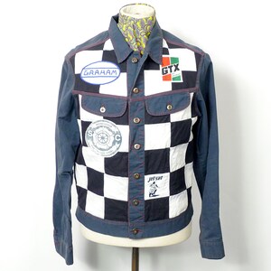 May include: A blue denim jacket with a checkered pattern in black and white. The jacket has several patches, including "Graham", "GTX", and "Jet Set" patches.