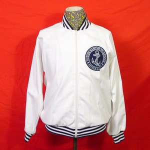 May include: White zippered jacket with blue and white striped cuffs and collar. The jacket has a blue embroidered patch with an anchor and the text "REGION MARITIME ATLANTIQUE SERVICE O.C.I.C."