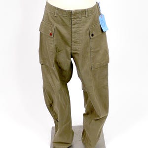 May include: A pair of olive green cargo pants with a herringbone pattern. The pants have two large cargo pockets on each leg and a button fly.