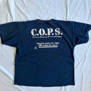May include: Navy blue t-shirt with white text that reads "C.O.P.S. Christians Obediently Preaching Salvation." Below the main text is the phrase "Wha'cha gonna do when HE comes for you?" The shirt is laid flat on a white surface.