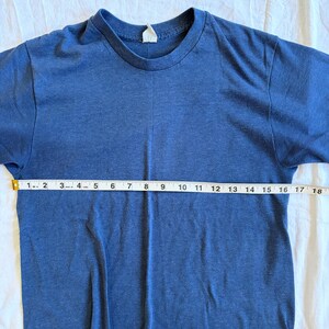 May include: A blue t-shirt with a crew neck. The shirt is measured with a tape measure, showing a length of approximately 18 inches. The fabric appears to be a soft, knit material.