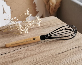 May include: A black whisk with a wooden handle engraved with the text "Pour la meilleure pâtissière" and a small heart.