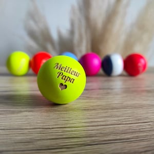 Peut inclure: Une balle verte brillante avec les mots "Meilleur Papa" et un cœur gravé à la surface. La balle est entourée d'autres balles colorées.