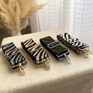 May include: Four different zebra print fabric straps with gold and silver clasps. The straps are all the same length and width, but have different color combinations of black, white, and green.