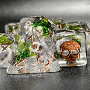 May include: Set of clear resin dice with embedded skulls, moss, and copper-colored numbering. The dice include a pyramid, cube, and other shapes, perfect for tabletop gaming.