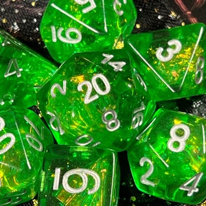 May include: Set of seven transparent green polyhedral dice with silver numbering. The dice are designed for tabletop role-playing games. The dice include a d4, d6, d8, d10, d12, d20, and a percentile die.