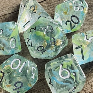 Puede incluir: Conjunto de seis dados translúcidos con remolinos verdes y azules y motas doradas. Los dados están numerados del 1 al 6.