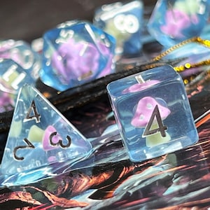 May include: A set of clear, blue-tinted dice with whimsical mushroom inclusions. The dice feature numbers and are designed for tabletop gaming. The mushrooms are pink and white, with green accents. The dice are a unique and colorful addition to any game.