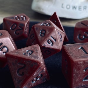 Puede incluir: Un conjunto de ocho dados rojos con números negros. Los dados son de varias formas y tamaños, incluyendo un d4, d6, d8, d10, d12 y d20.