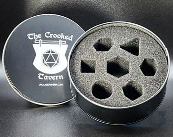 Pode incluir: Uma lata de metal preta com um interior de espuma para guardar dados. A tampa apresenta um logotipo branco que diz "The Crooked Tavern" com uma imagem estilizada de uma placa de taverna e um dado de 20 faces.