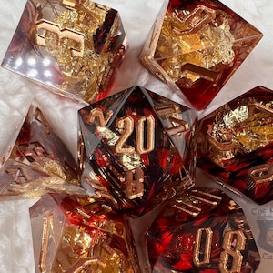 Pu&ograve; includere: Set di sette dadi poliedrici a tema rosso e oro. I dadi sono trasparenti con dettagli rossi e inclusioni di foglie d'oro. I numeri sono dorati. Per giochi da tavolo.