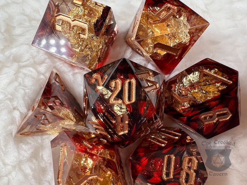 Pu&ograve; includere: Set di sette dadi poliedrici a tema rosso e oro. I dadi sono trasparenti con dettagli rossi e inclusioni di foglie d'oro. I numeri sono dorati. Per giochi da tavolo.