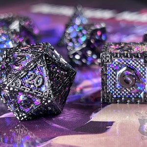May include: A set of black and iridescent dice with a glittery finish. The dice are in the shape of a d20, d6, and d4. The dice are on a purple surface.