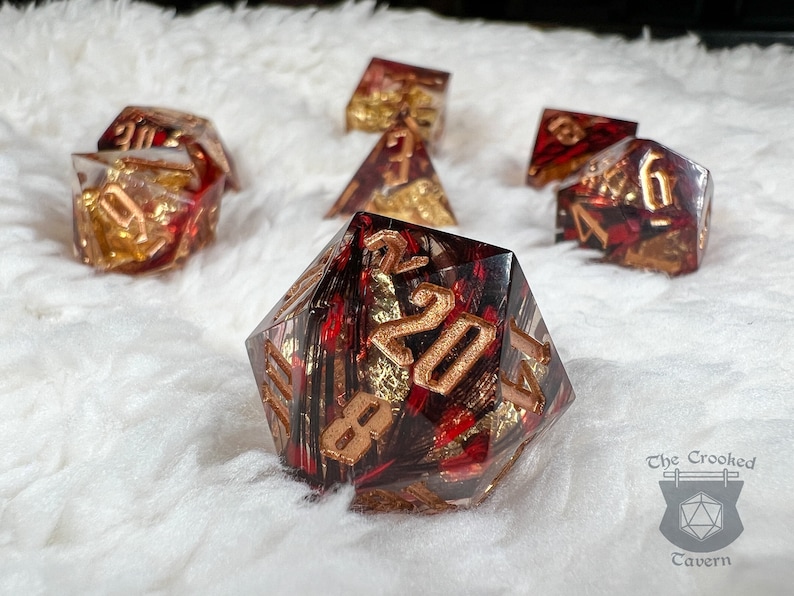 Pu&ograve; includere: Set di dadi poliedrici rossi e dorati. I dadi sono realizzati in resina trasparente con scaglie rosse e dorate e numeri dorati. Per giochi da tavolo.