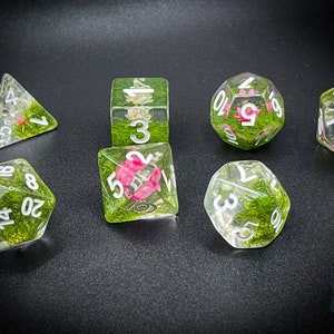 May include: Set of seven clear dice with green and pink floral accents. The dice are numbered 1-10 and include a d4, d6, d8, d10, d12, and d20.