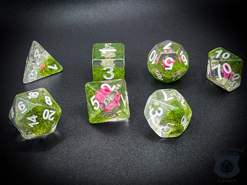 May include: Set of seven clear dice with green and pink floral accents. The dice are numbered 1-10 and include a d4, d6, d8, d10, d12, and d20.