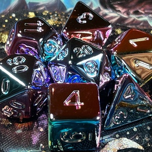 May include: A set of iridescent metal dice in various shapes and sizes. The dice are a mix of purple, blue, and green colors with silver numbers. The dice are on a black background with gold glitter.