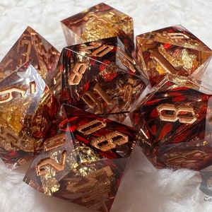 Pu&ograve; includere: Set di sette dadi poliedrici. Ogni dado &egrave; trasparente con inclusioni rosse e dorate e numerazione dorata. I dadi sono progettati per giochi di ruolo da tavolo.