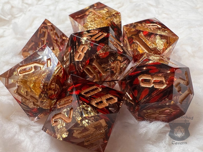 Pu&ograve; includere: Set di sette dadi poliedrici. Ogni dado &egrave; trasparente con inclusioni rosse e dorate e numerazione dorata. I dadi sono progettati per giochi di ruolo da tavolo.