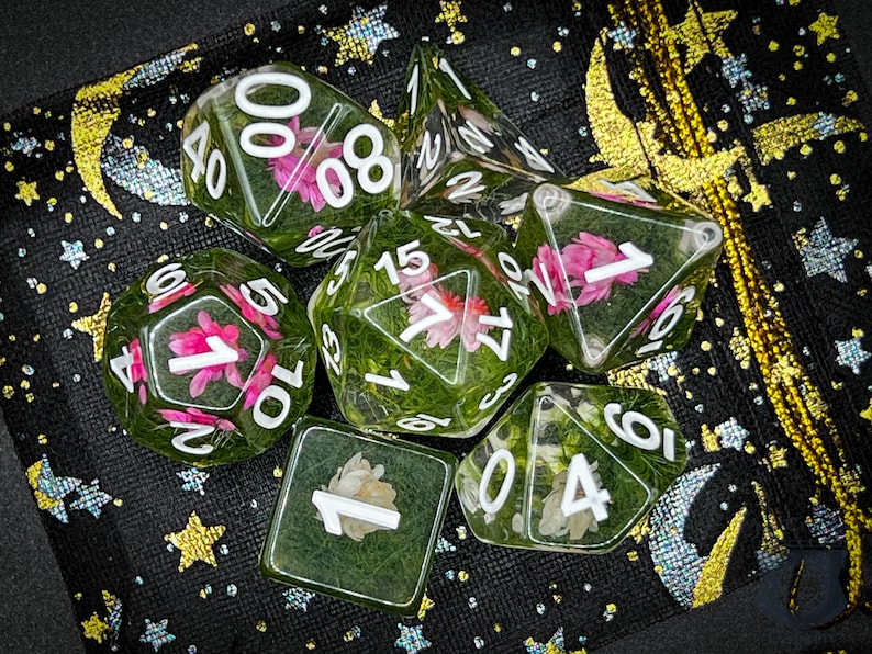 May include: A set of six clear dice with green and white floral accents. The dice are on a black background with gold stars and moons.