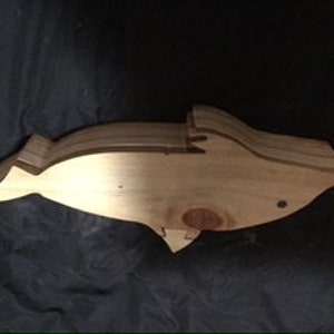 May include: A wooden dolphin sculpture, carved from light brown wood. The dolphin is in a horizontal position, with its tail and fins visible.