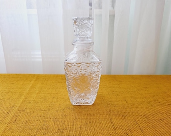 May include: A clear glass decanter with a textured surface and a stopper. The decanter is sitting on a yellow tablecloth.