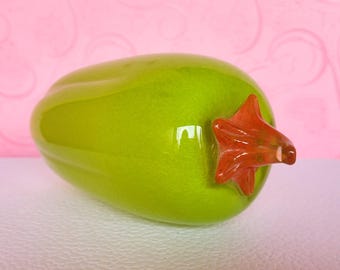 May include: A green glass pepper with a red glass stem. The pepper is smooth and shiny, and the stem is detailed with a swirl pattern.