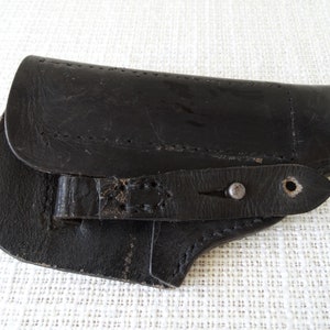 Könnte beinhalten: Schwarzes Lederholster mit einem Metall-Druckknopfverschluss und einem Riemen zum Befestigen an einem Gürtel.