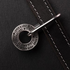 May include: A silver dog tag with the text "PO19  ARO  CALL  PLEASE  -  WATER  ROAD" and "LOVED & LOST  T.S.  130  CHIPPED  07709  1941891" engraved on it. The tag is attached to a brown leather dog collar.