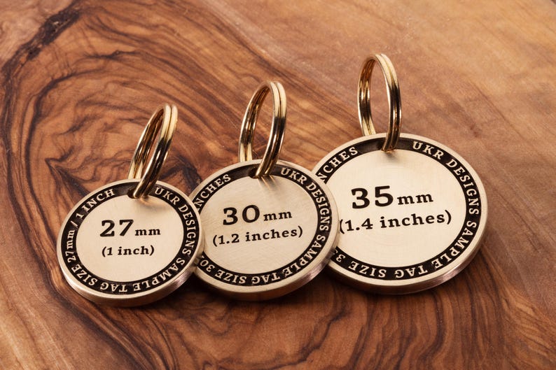 May include: Three brass keyrings with different sizes, 2.5 cm, 3 cm, and 3.5 cm. Each keyring has a round tag with the size printed in millimetres and inches. The text on the tag reads "UKR DESIGNS SAMPLE TAG SIZE".