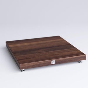 May include: A dark brown wooden audio equipment stand with four silver feet. The stand has a small silver logo on the front.