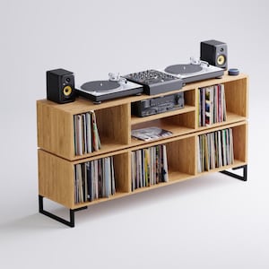 Op de afbeelding: Een houten platenspelerstandaard met zwarte metalen poten. De standaard heeft planken om vinylplaten op te bergen en ruimte voor een draaitafel en een versterker. De standaard is gemaakt van licht hout en heeft een modern ontwerp.