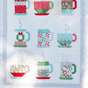 May include: A white quilt with a patchwork design of nine colorful mugs. Each mug is made of different fabrics and patterns, including red, green, blue, and white. The mugs are arranged in a 3x3 grid.