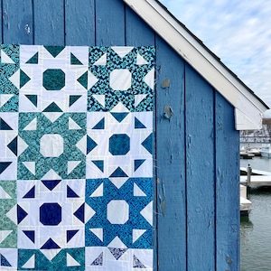 May include: A blue and white quilt with a star pattern. The quilt is hanging on a blue wooden wall.