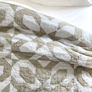 May include: A beige and white geometric patterned quilt with a textured surface. The quilt is folded over a white bed.