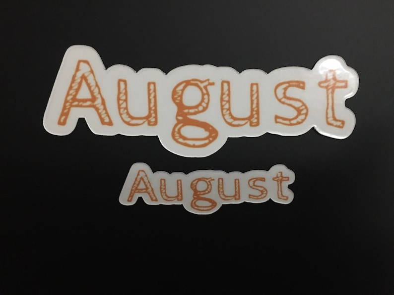 May include: Two white stickers with the word "August" written in orange. The top sticker is larger and has a more stylized font.