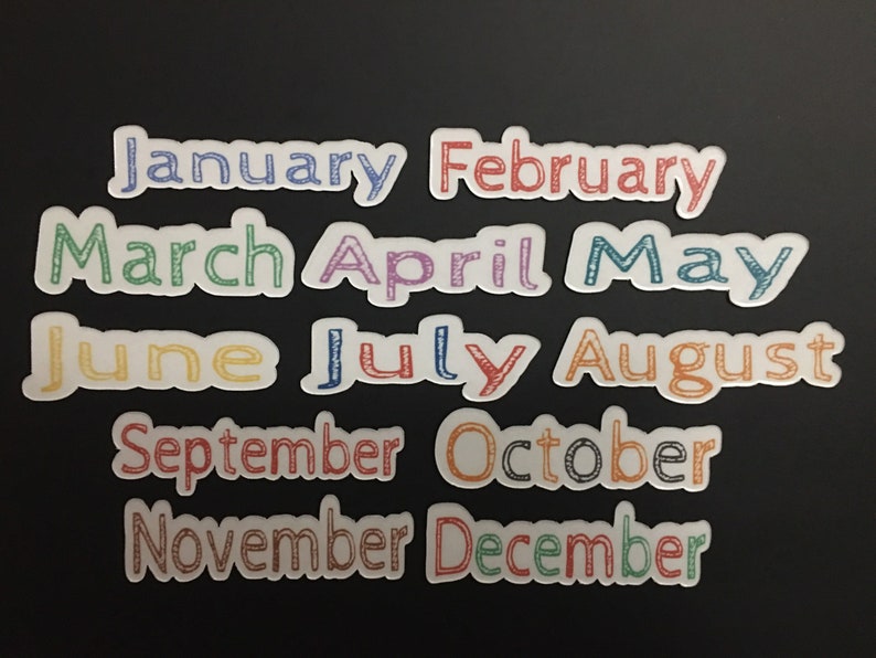 May include: Twelve white stickers with the months of the year written in colorful, handwritten-style font. The stickers are arranged in three rows of four stickers each.