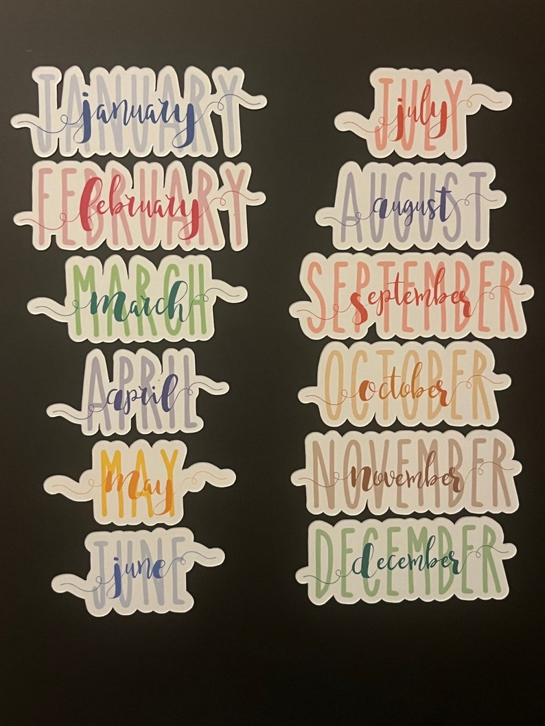 Puede incluir: Doce pegatinas coloridas, cada una con el nombre de un mes del a&ntilde;o escrito a mano. Las pegatinas son de colores pastel como azul, rosa, verde y amarillo, sobre un fondo negro. Ideales para planificadores.