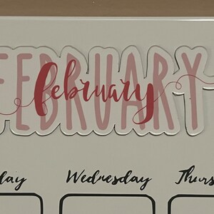 Puede incluir: Una pegatina transparente con la palabra "FEBRUARY" en letras rosas y una superposici&oacute;n de "february" en cursiva. La pegatina se coloca encima de los d&iacute;as de la semana sobre un fondo blanco.