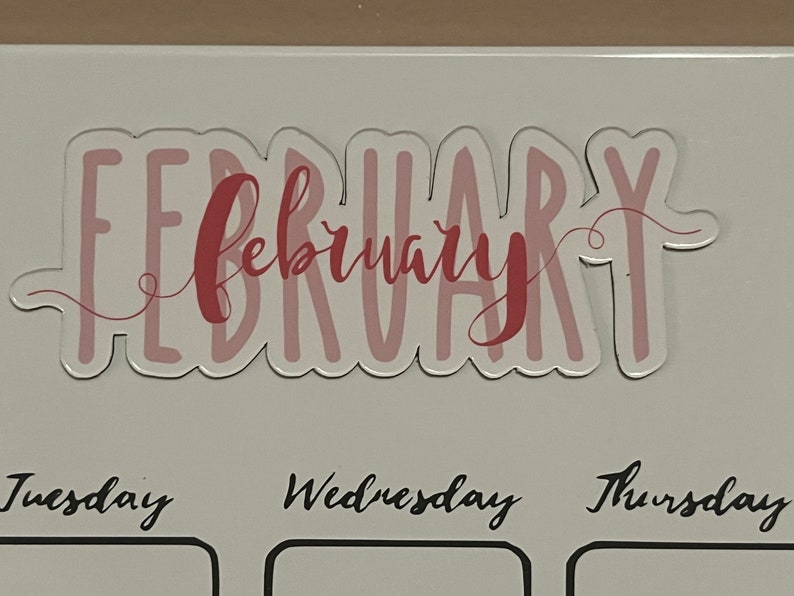 Puede incluir: Una pegatina transparente con la palabra "FEBRUARY" en letras rosas y una superposici&oacute;n de "february" en cursiva. La pegatina se coloca encima de los d&iacute;as de la semana sobre un fondo blanco.