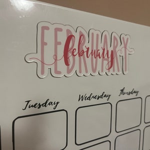 Puede incluir: Primer plano de un calendario blanco con el mes de febrero resaltado. La palabra "February" est&aacute; escrita en escritura rosa con un contorno rosa claro. Los d&iacute;as de la semana est&aacute;n escritos en escritura negra.