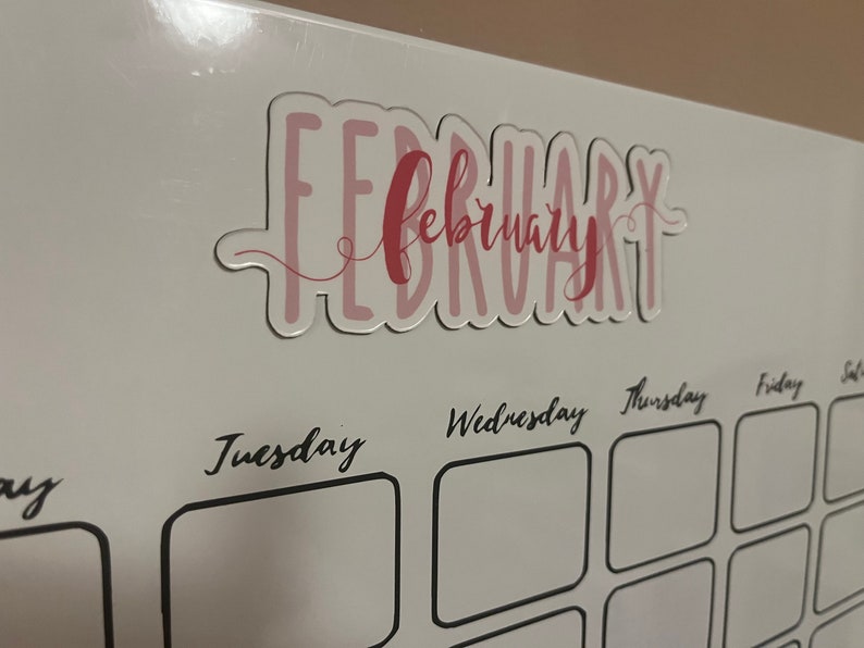 Puede incluir: Primer plano de un calendario blanco con el mes de febrero resaltado. La palabra "February" est&aacute; escrita en escritura rosa con un contorno rosa claro. Los d&iacute;as de la semana est&aacute;n escritos en escritura negra.