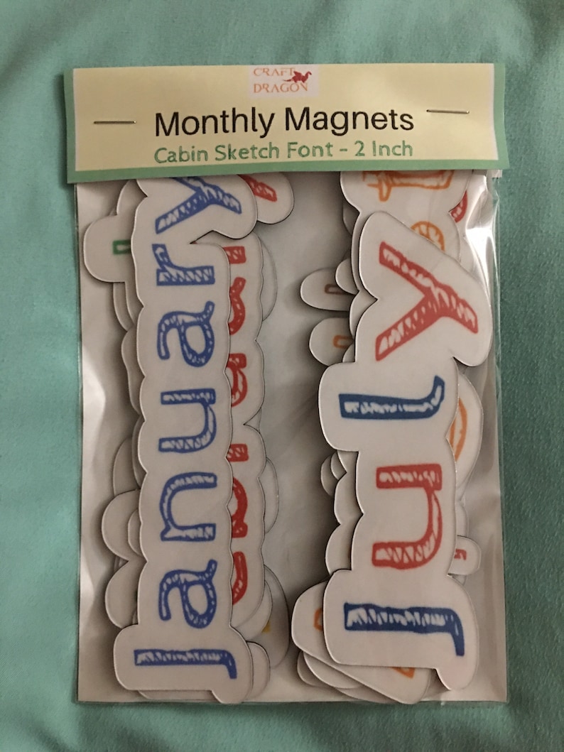 May include: A set of 2-inch magnetic letters in a cabin sketch font. The letters are in various colors, including blue, red, orange, and green. The letters are arranged in a pile, with the letters "January" and "July" visible.