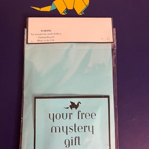 Puede incluir: Un paquete azul claro con el texto "your free mystery gift" y un drag&oacute;n de origami de papel. El paquete incluye una etiqueta de advertencia que dice "Not intended for small children. Choking Hazard! Made in the USA."