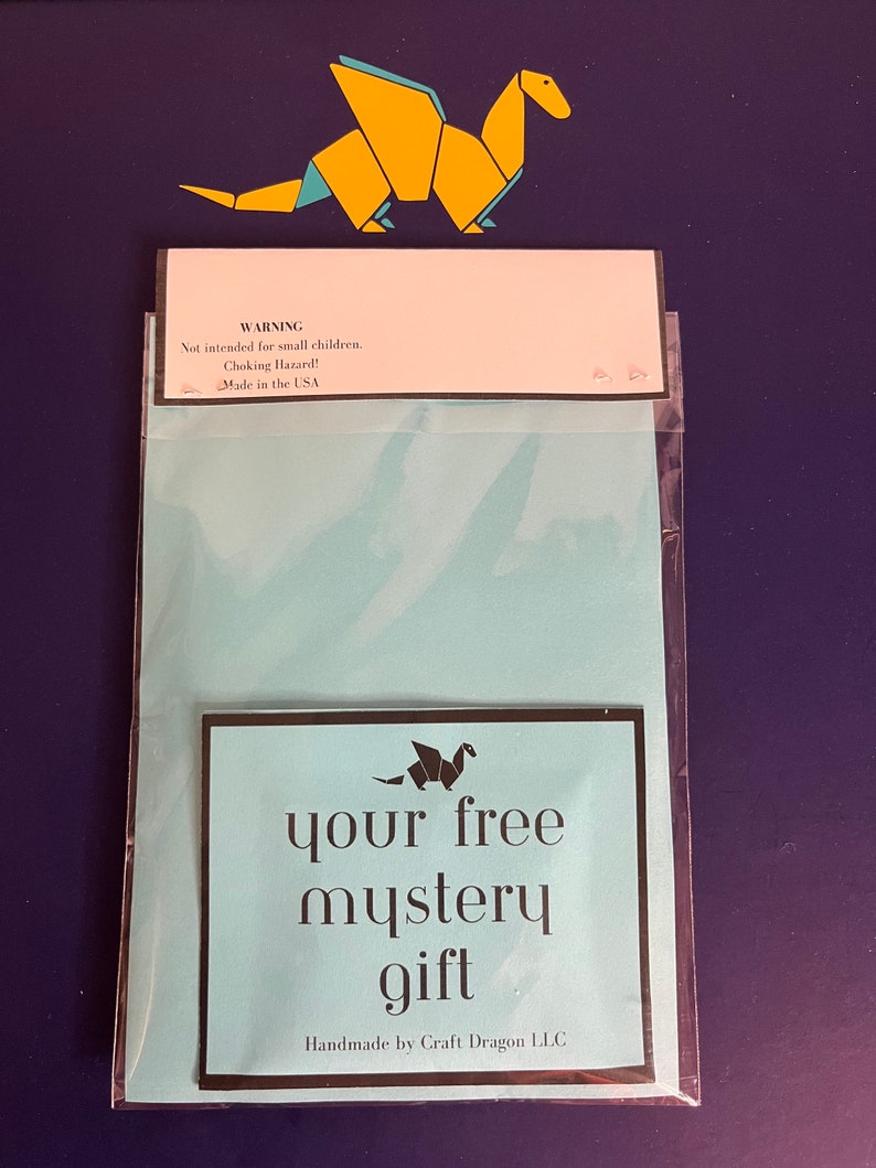 Puede incluir: Un paquete azul claro con el texto "your free mystery gift" y un drag&oacute;n de origami de papel. El paquete incluye una etiqueta de advertencia que dice "Not intended for small children. Choking Hazard! Made in the USA."