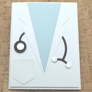 May include: A handmade greeting card featuring a doctor's coat design. The card is white with a light blue lapel and pocket. A black stethoscope with silver accents is also included in the design.