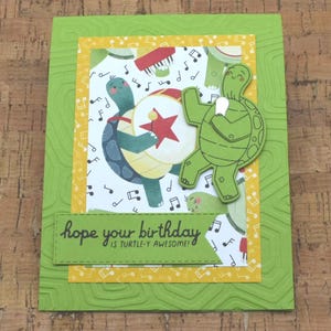 May include: Green card with a yellow border and a white background with musical notes and two turtles. One turtle is playing a drum and the other is holding a microphone. The card says "hope your birthday is turtle-y awesome!"