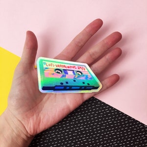 May include: A holographic sticker of a cassette tape with the text "LOFI-VAPORWAVE-24/7" on it.